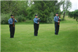 Three officers in uniform standing at attention with  rifles in hand in grass