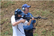 Officer standing beside young man shooting a rifle