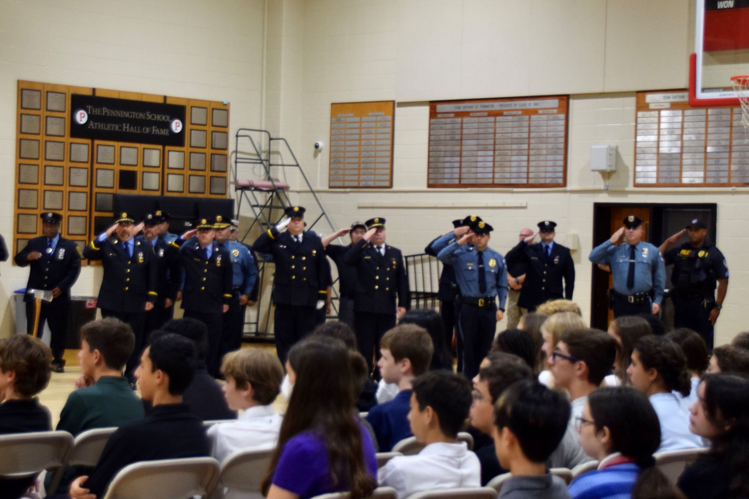 Photo of police and firefighters saluting in a gym with students in chairs